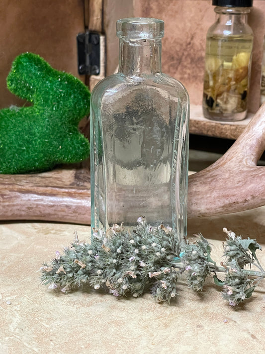 Antique 3-in-One light blue glass apothecary bottle shown on a lace-covered table in soft candlelight. Photographed at different angles to highlight the embossed text, paneled shape, and worn clarity.