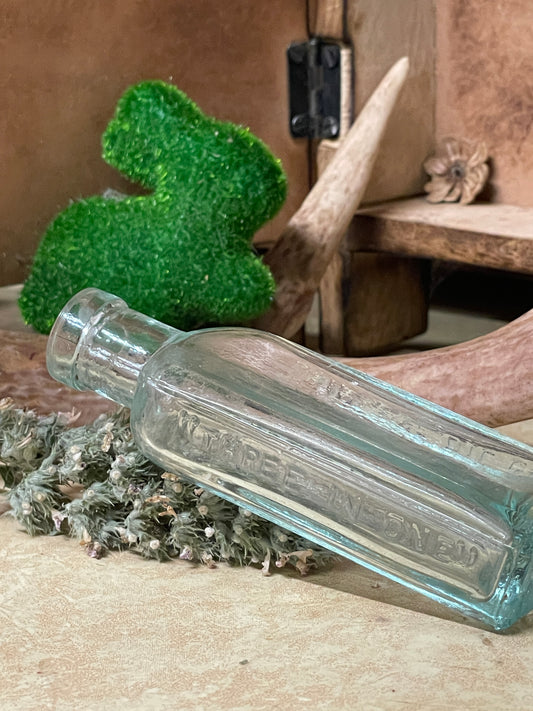 Antique 3-in-One light blue glass apothecary bottle shown on a lace-covered table in soft candlelight. Photographed at different angles to highlight the embossed text, paneled shape, and worn clarity.