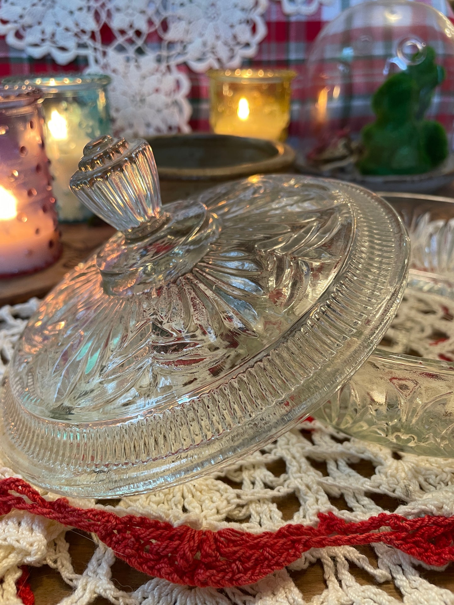 Vintage 1960s Avon Crystalique powder dish with a pressed glass design and elegant finial, styled on a red and white crochet doily with lit candles.