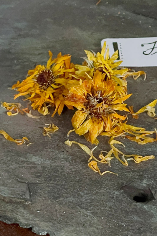 Dried calendula flowers on slate, showing golden petals and natural texture from Lizzy Lane Farm herbal cabinet