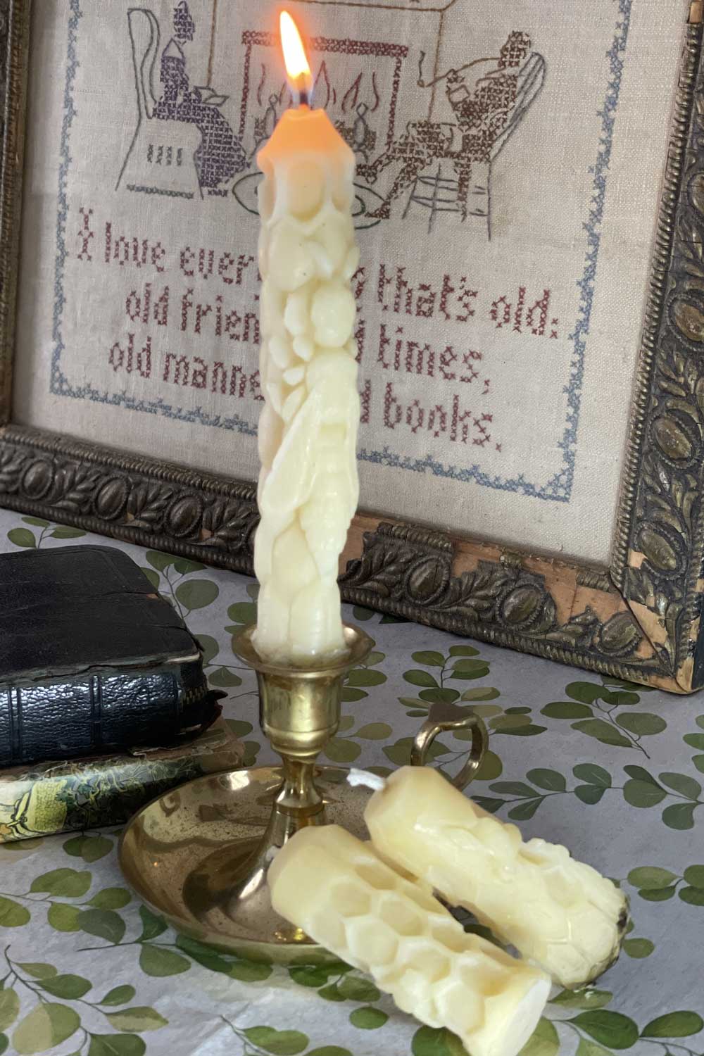 a beeswax tapered candle with bee and honeycomb details gently glowing wit the mini version resting close by. beeswax candle by lizzy lane farm.