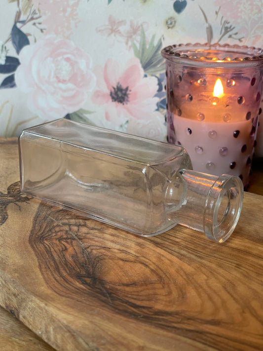 Antique thick glass square apothecary bottle photographed on a lace-covered table under candlelight. Shown from various angles to highlight thick glass texture, slight clouding, and hand-applied lip.