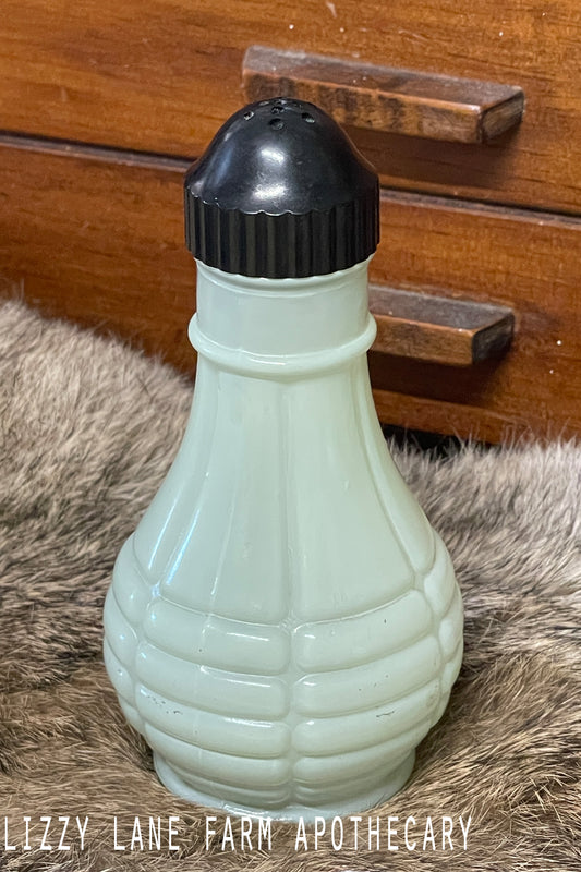 Vintage Anchor Hocking fired-on jadeite green salt shaker with ribbed pattern and bakelite lid photographed on a lace-covered table under candlelight. Multiple angles show the soft color and vintage condition.