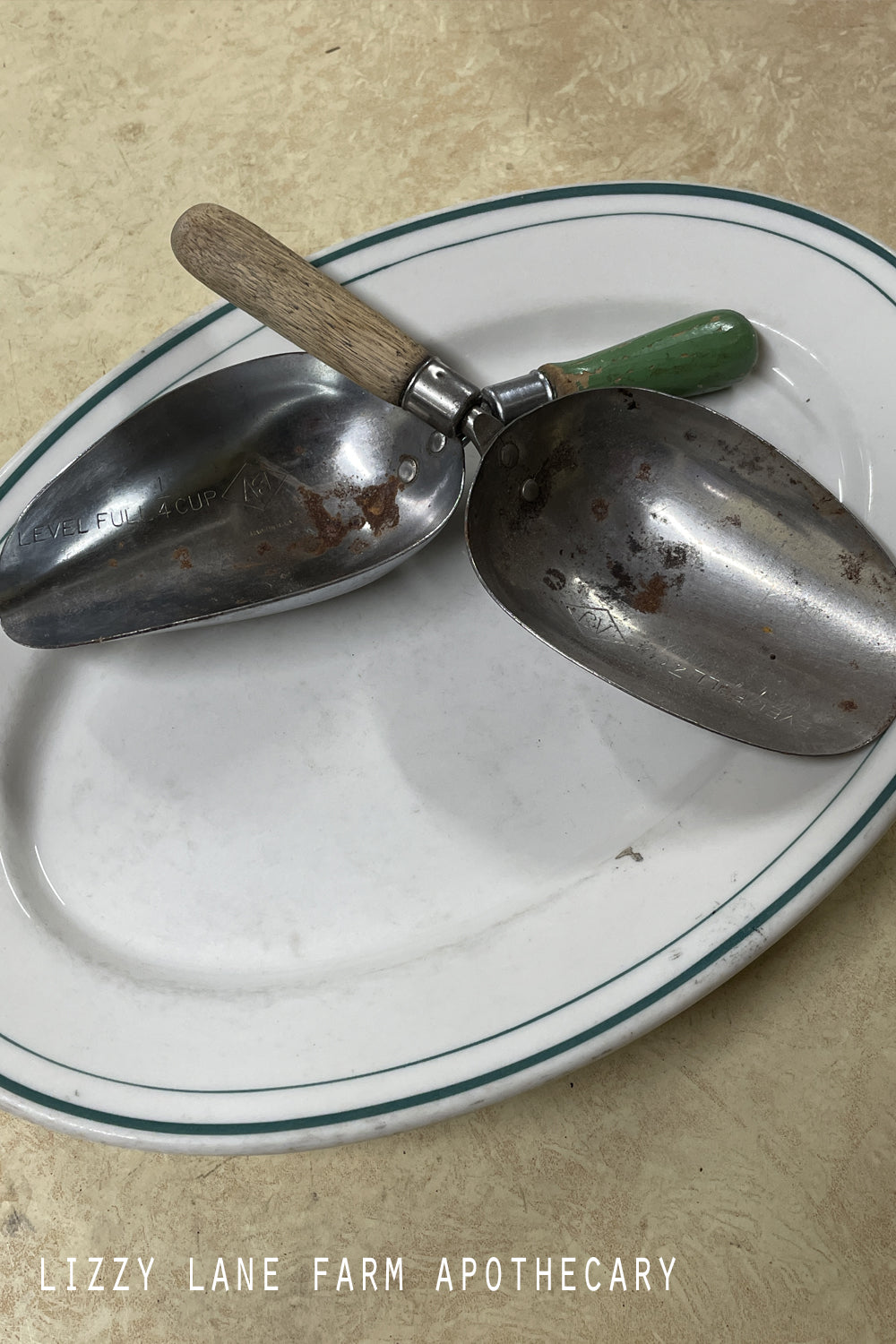 Set of two vintage A & J 1/4 cup measuring scoops with silver metal cups and worn painted wooden handles photographed on a farmhouse lace table with candlelight. Multiple angles highlight patina and markings.