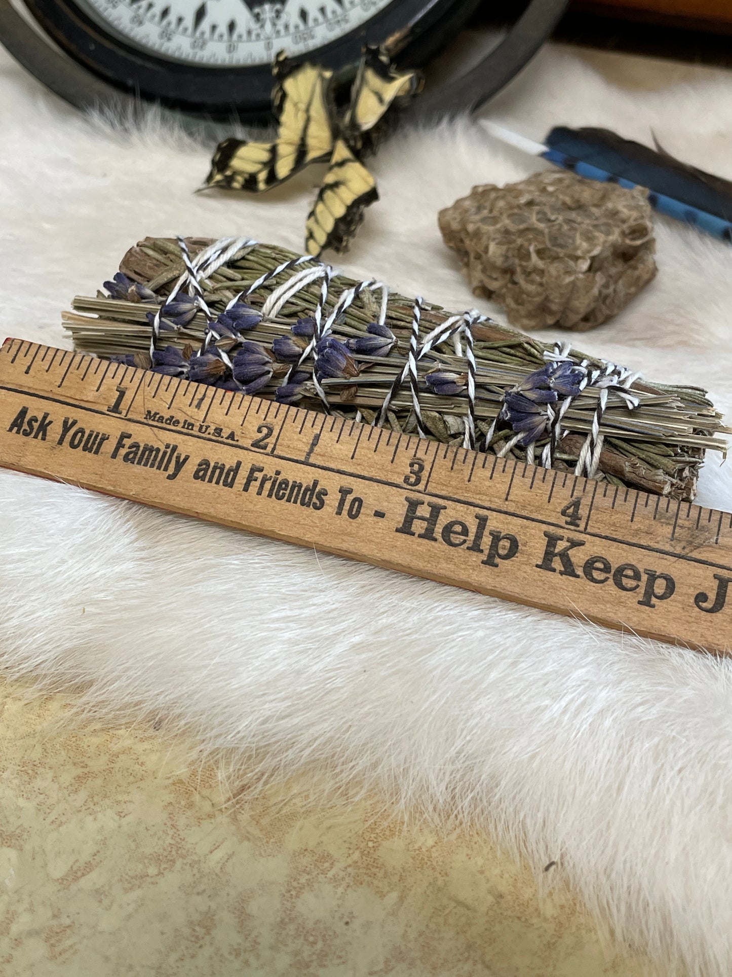 a ruler sitting next to the hand tied lavender and rosemary herb bundle. all resting on a white fur