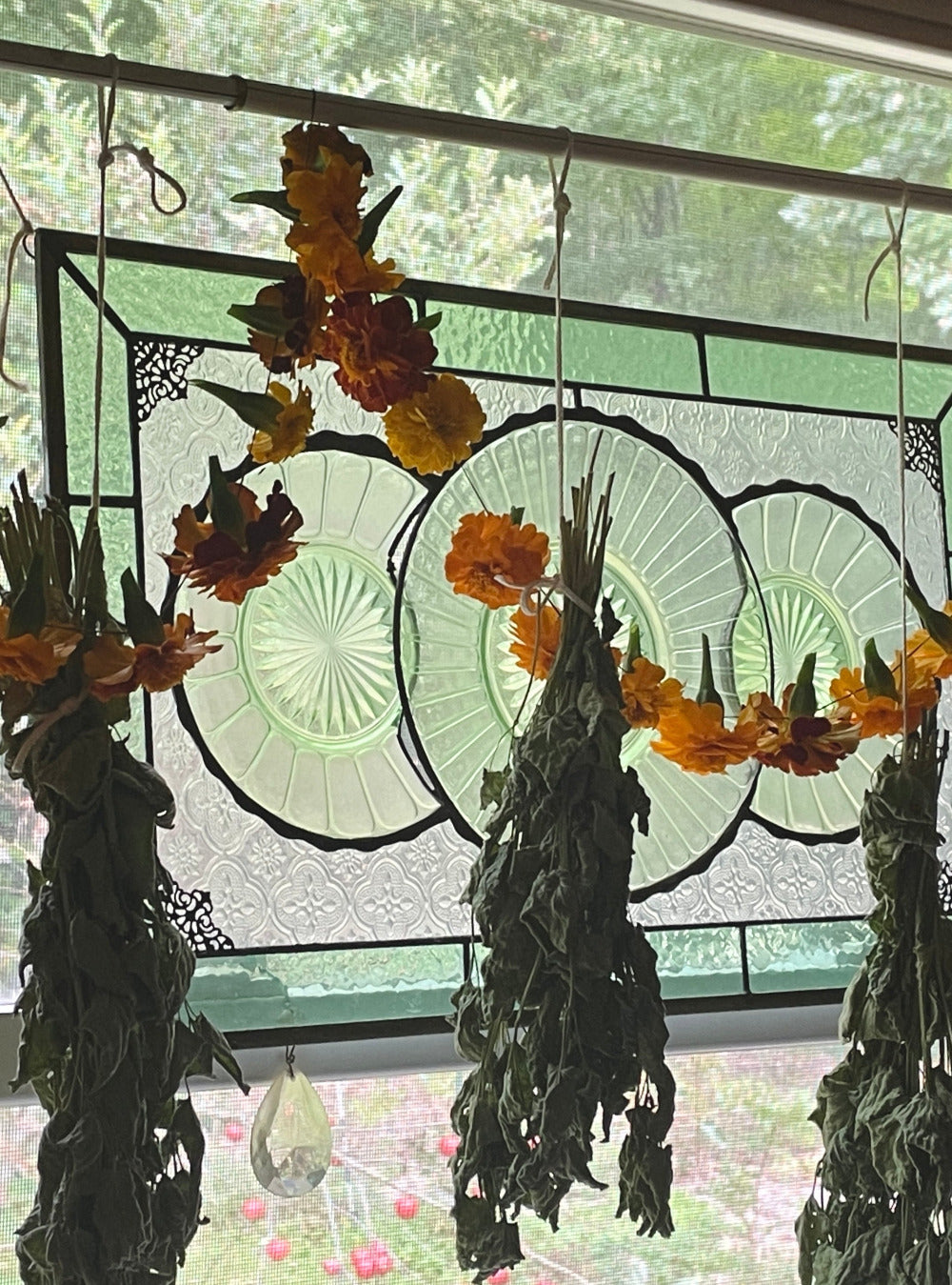 a peek out the stillroom window, where stained glass and merigold garlands hang along side drying herbs.