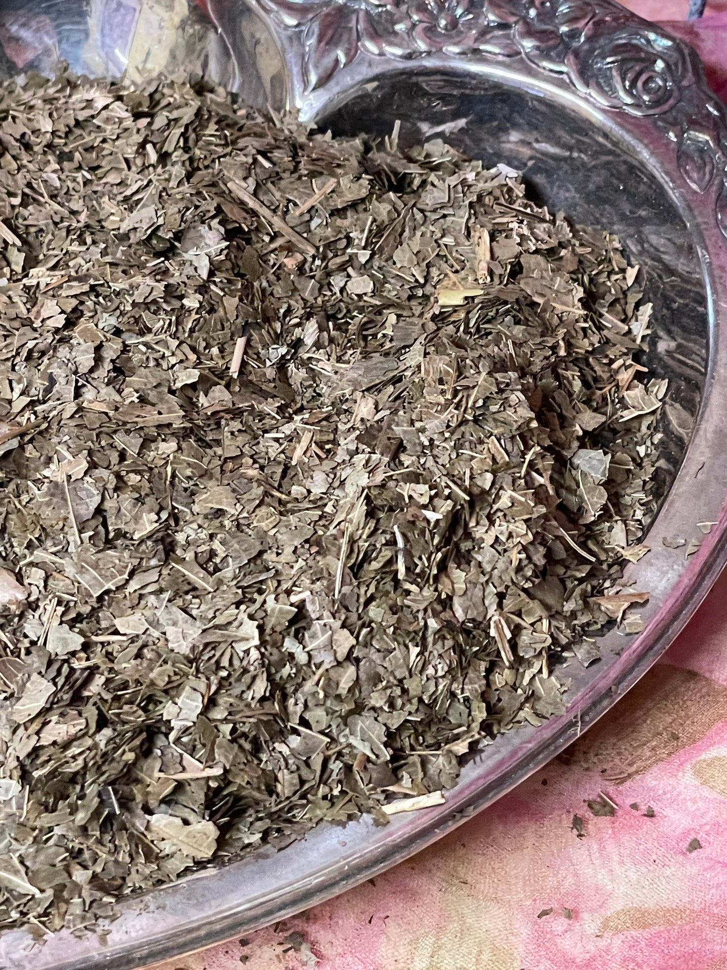 Close-up of cut organic black walnut leaves displayed in a vintage silver-plated bowl, showcasing the textured leaves and rich green color.