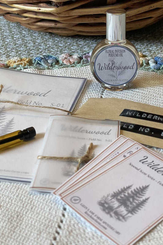 The wildwood perfume part of the seasonal floral infused collection. Both the large and sample sized field guide cards and perfume bottles resting on a vintage linen.