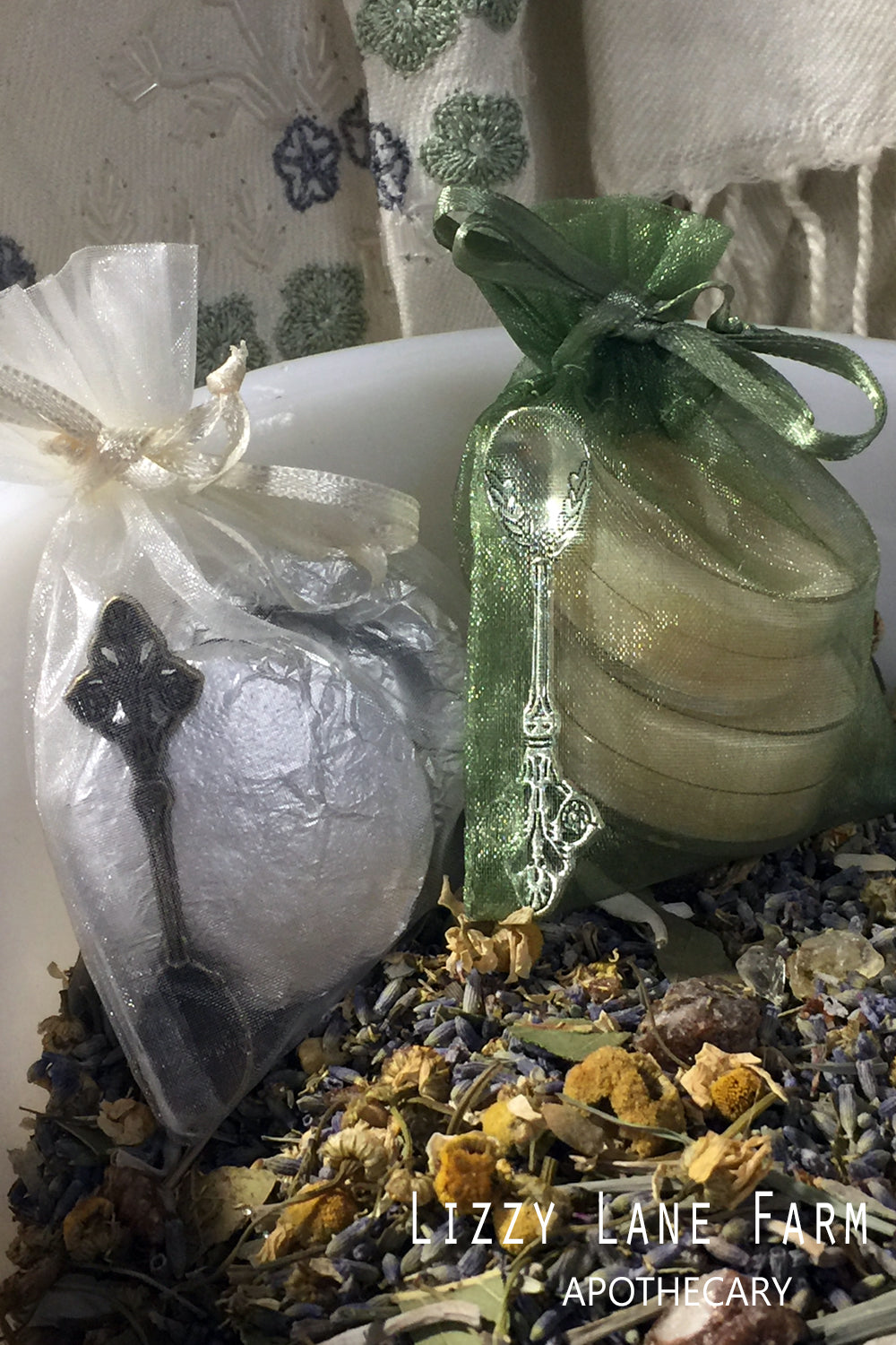 A beautifully arranged incense accessory kit featuring a green organza bag holding a herbal metal spoon and a charcoal briquet. Beside it, a white organza bag contains a handmade beeswax tea light candle and another herbal metal spoon, both nestled on a bed of calming herbs. Perfect for enhancing your incense burning experience.