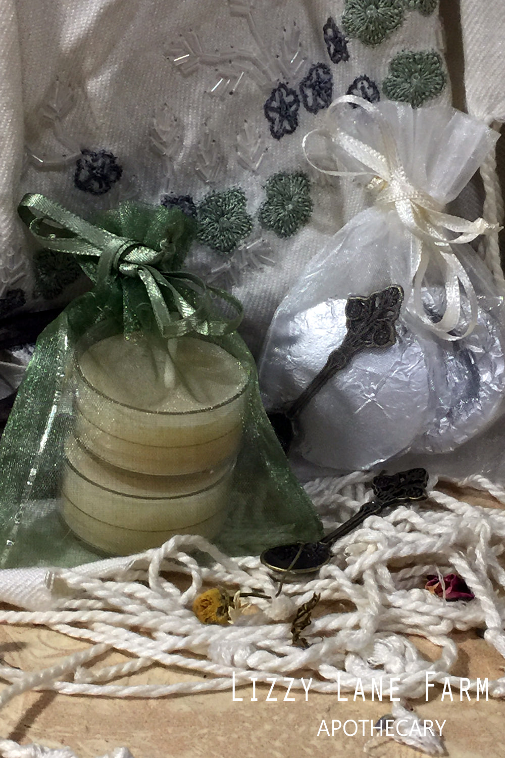 A beautifully arranged incense accessory kit featuring a green organza bag holding a herbal metal spoon and a charcoal briquet. Beside it, a white organza bag contains a handmade beeswax tea light candle and another herbal metal spoon, both nestled on a bed of calming herbs. Perfect for enhancing your incense burning experience.