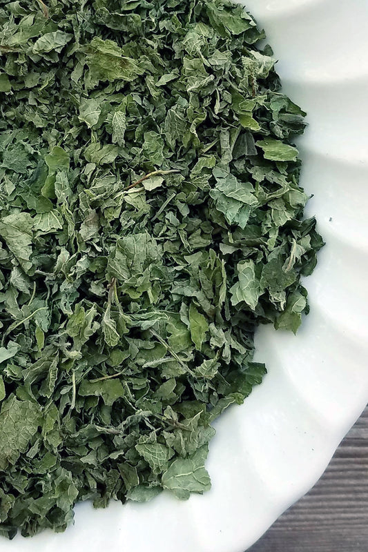 A close-up of dried and cut lemon balm leaves in a rustic wooden bowl, showcasing the fresh, green texture of the herb.
