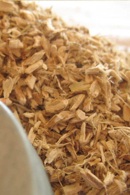 A rustic bowl filled with dried, small cut marshmallow root, resting on a wooden table.