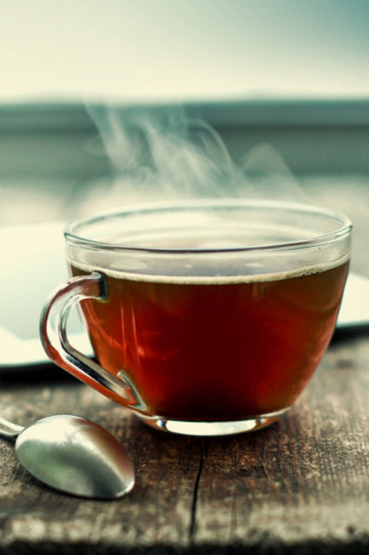 Steaming cup of tea placed on a wooden table, with dried herbs scattered around, evoking a calm and soothing atmosphere.
