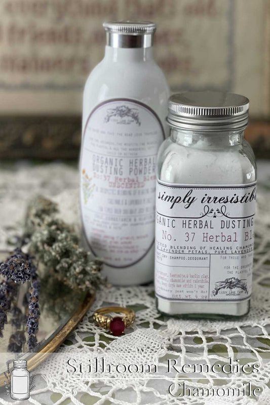 Two jars of herbal dusting powder—one in a glass shaker, the other in a white aluminum bottle—rest on lace with dried lavender and a vintage ring. A soft, natural scene that evokes the charm and care of Lizzy Lane Farm’s Stillroom Remedies.