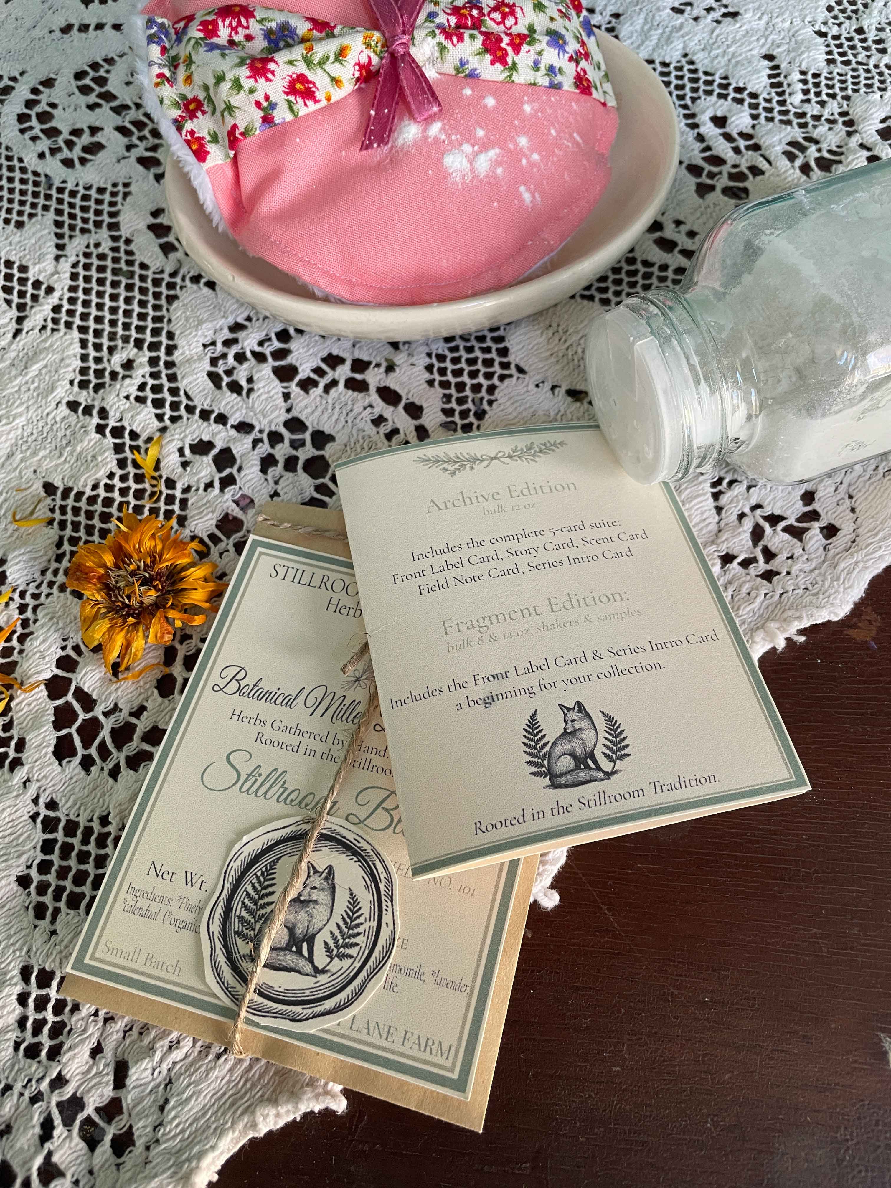 Stillroom Blend Herbal Dusting Powder sample in a kraft coin envelope with Archive Series Intro card, shown beside a vintage powder puff — part of the Herb & Oil Infused collection.
