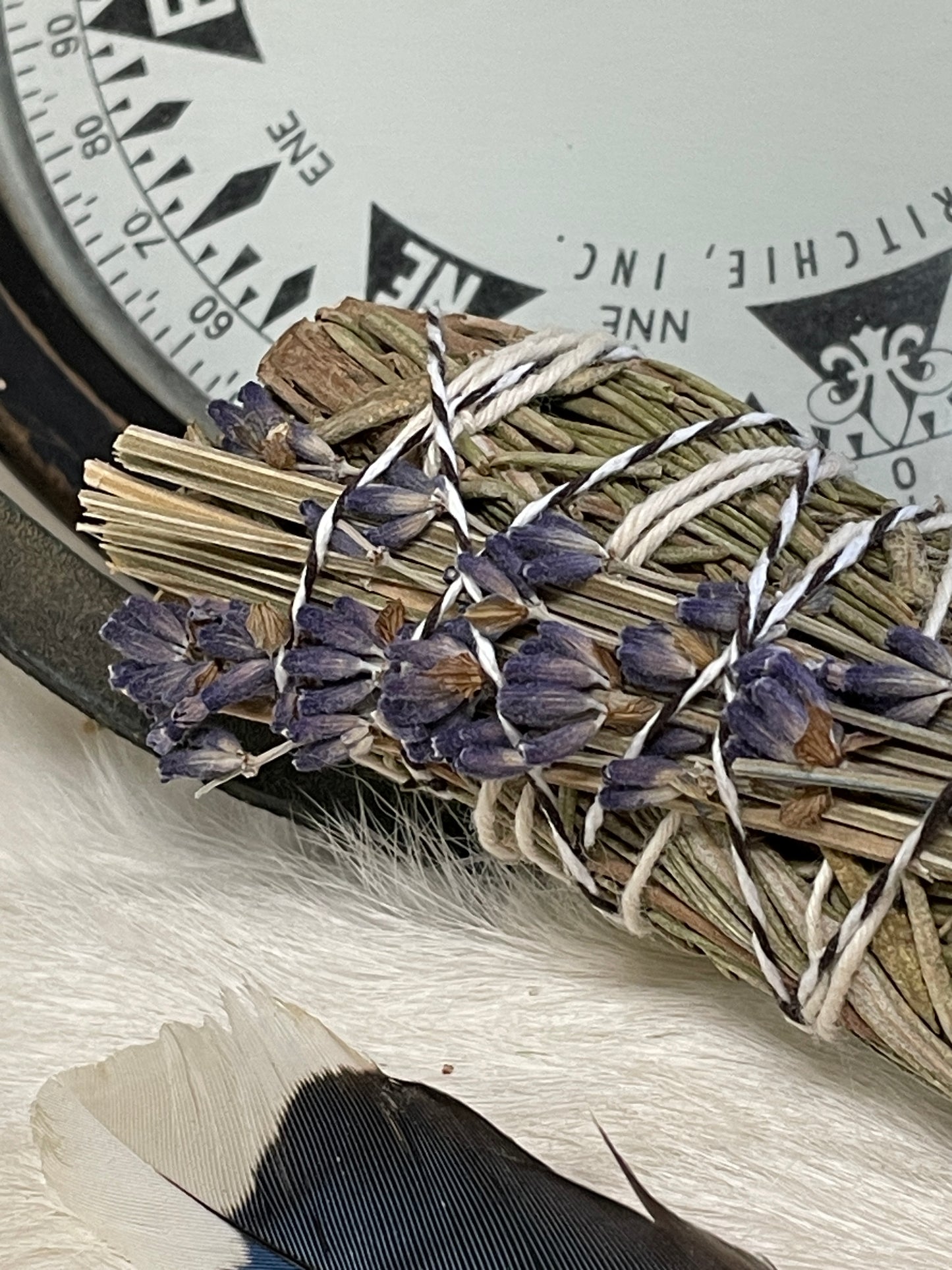 a close up showing details of the hand tied rosemary and lavender herb bundle with a bird feather laying close by.
