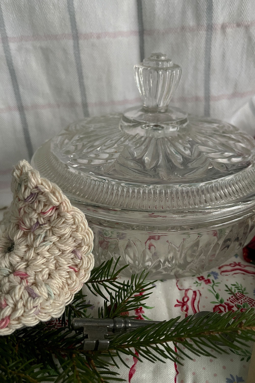 Close-up of vintage Avon Crystalique pressed-glass powder dish with crocheted powder puff and evergreen sprig — a winter vanity keepsake.