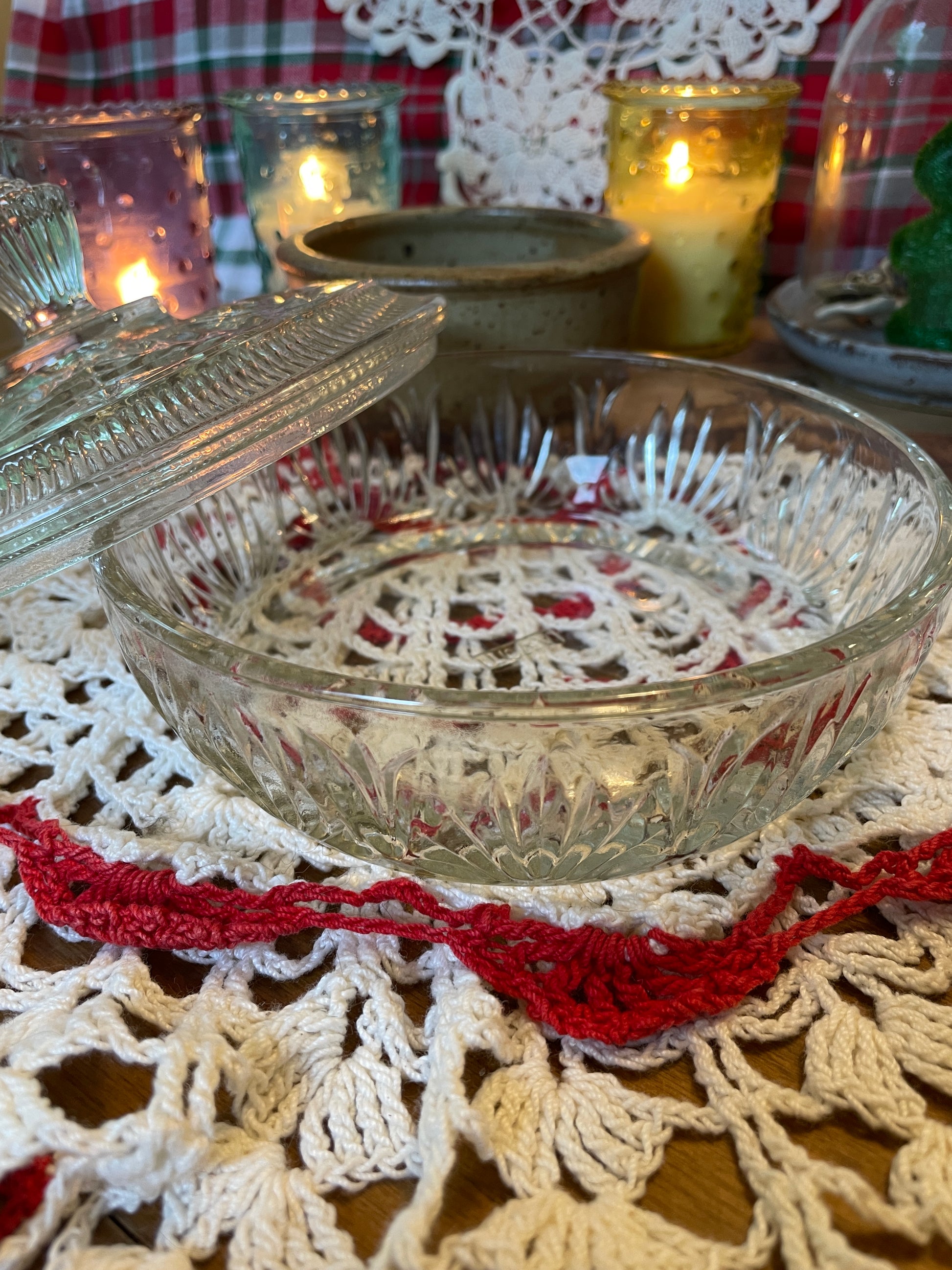 Vintage 1960s Avon Crystalique powder dish with a pressed glass design and elegant finial, styled on a red and white crochet doily with lit candles.