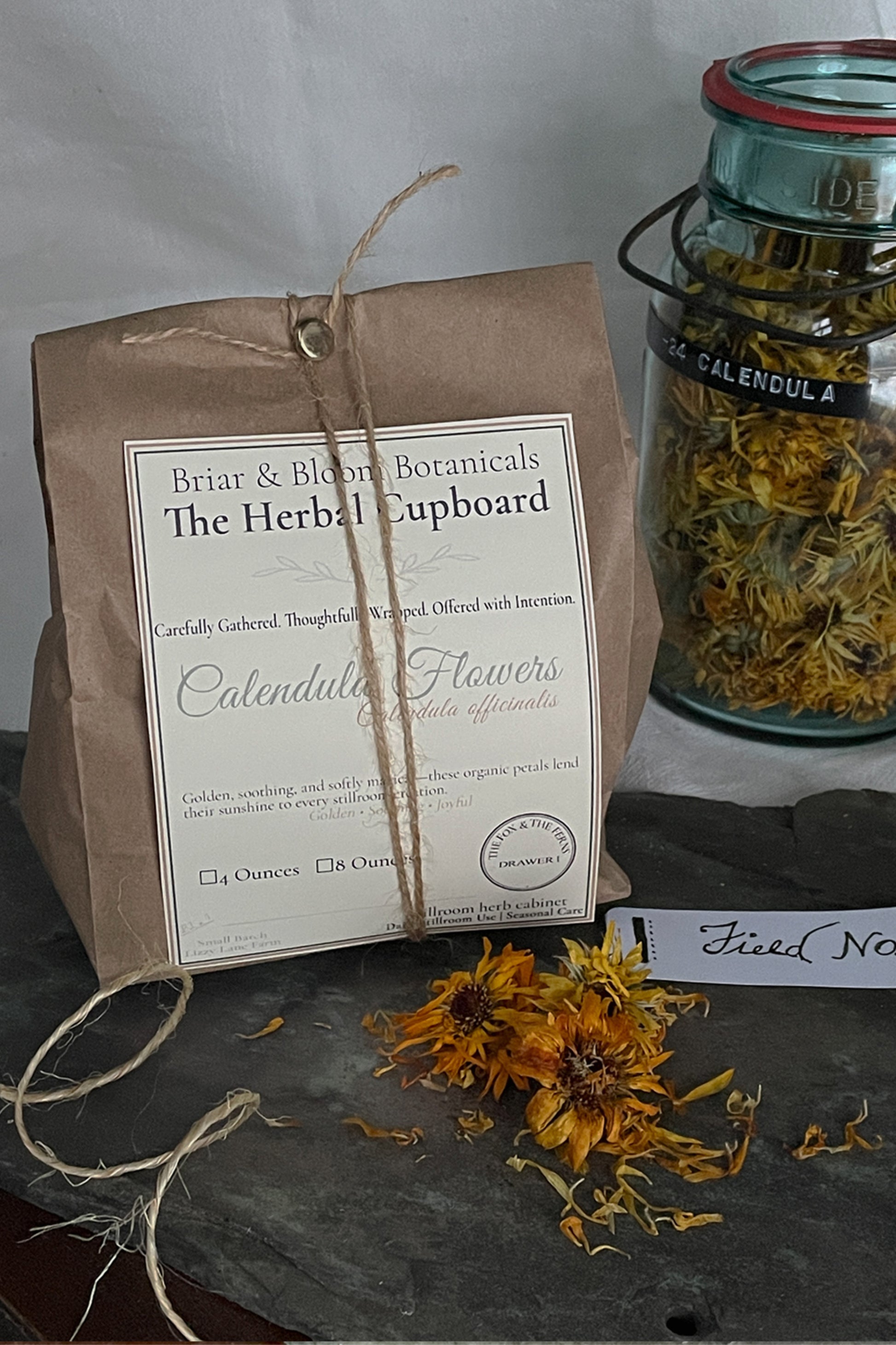Packaged dried calendula flowers in kraft paper bag and glass jar, Lizzy Lane Farm herbal cupboard offering
