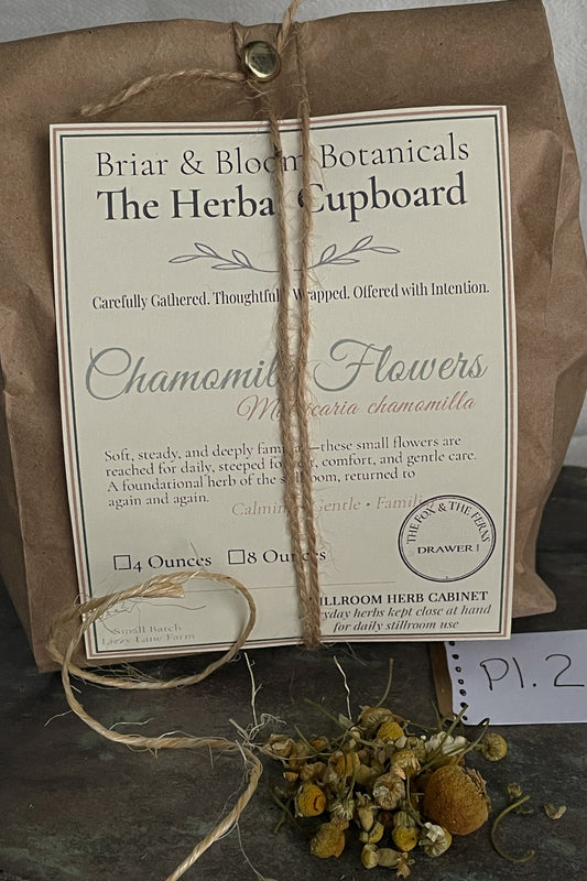 Loose chamomile flowers packaged in a brown paper bag with twine and botanical label, from the Stillroom Herb Cabinet at Lizzy Lane Farm
