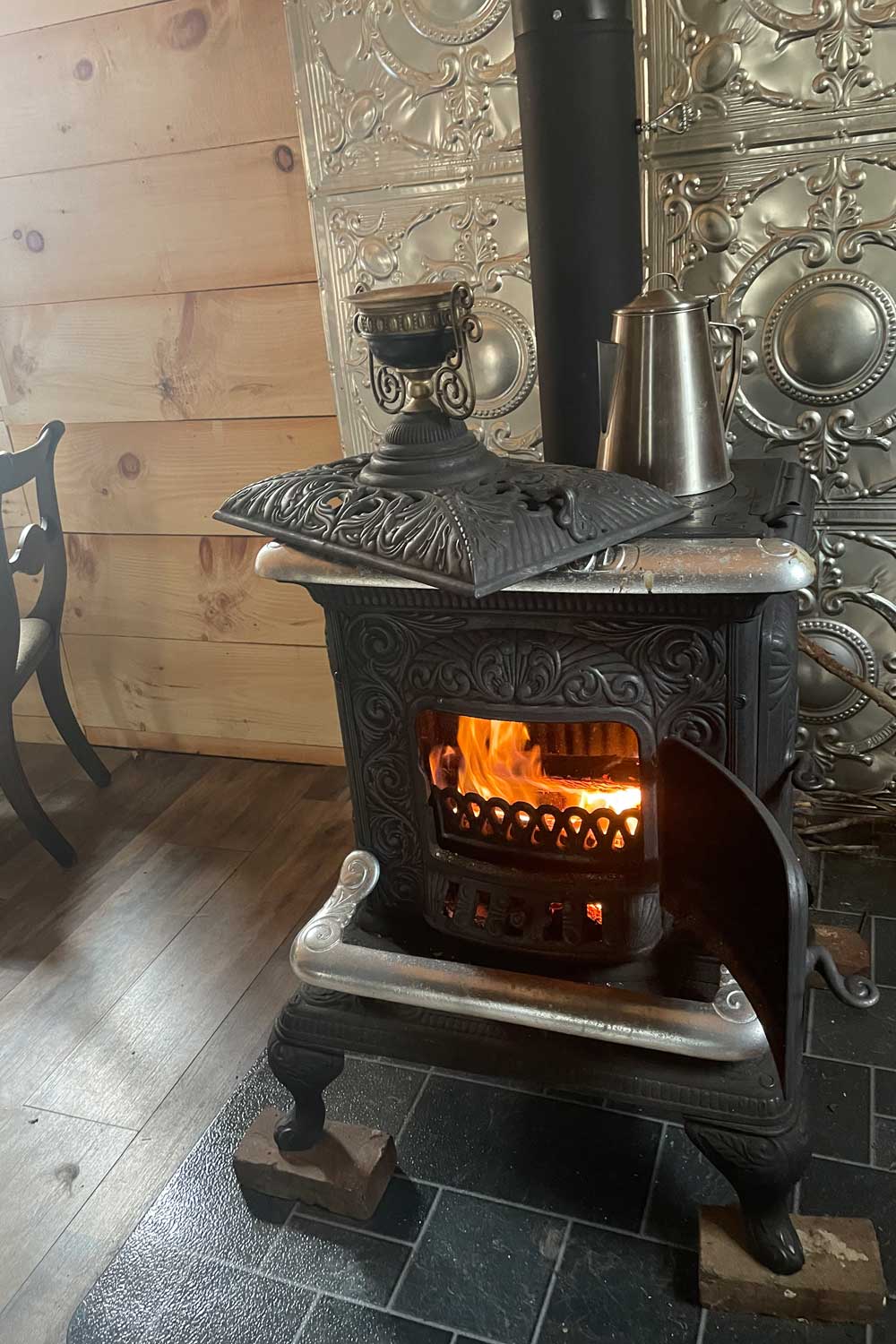 Ornate cast-iron cook stove with fire glowing and a pot heating on top — farmhouse kitchen comfort of oats, honey, and cider
