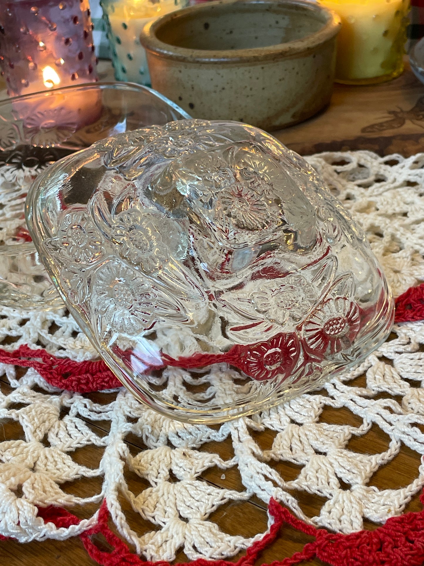 Vintage pressed glass powder dish with daisy motif, photographed on red and white crochet doily with lit candles in the background – top view showcasing lid detail.