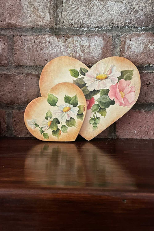 Vintage heart-shaped decorative items with floral designs against a brick wall.