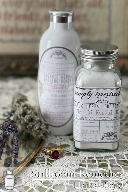 Two jars of herbal dusting powder—one in a glass shaker, the other in a white aluminum bottle—rest on lace with dried lavender and a vintage ring. A soft, natural scene that evokes the charm and care of Lizzy Lane Farm’s Stillroom Remedies.