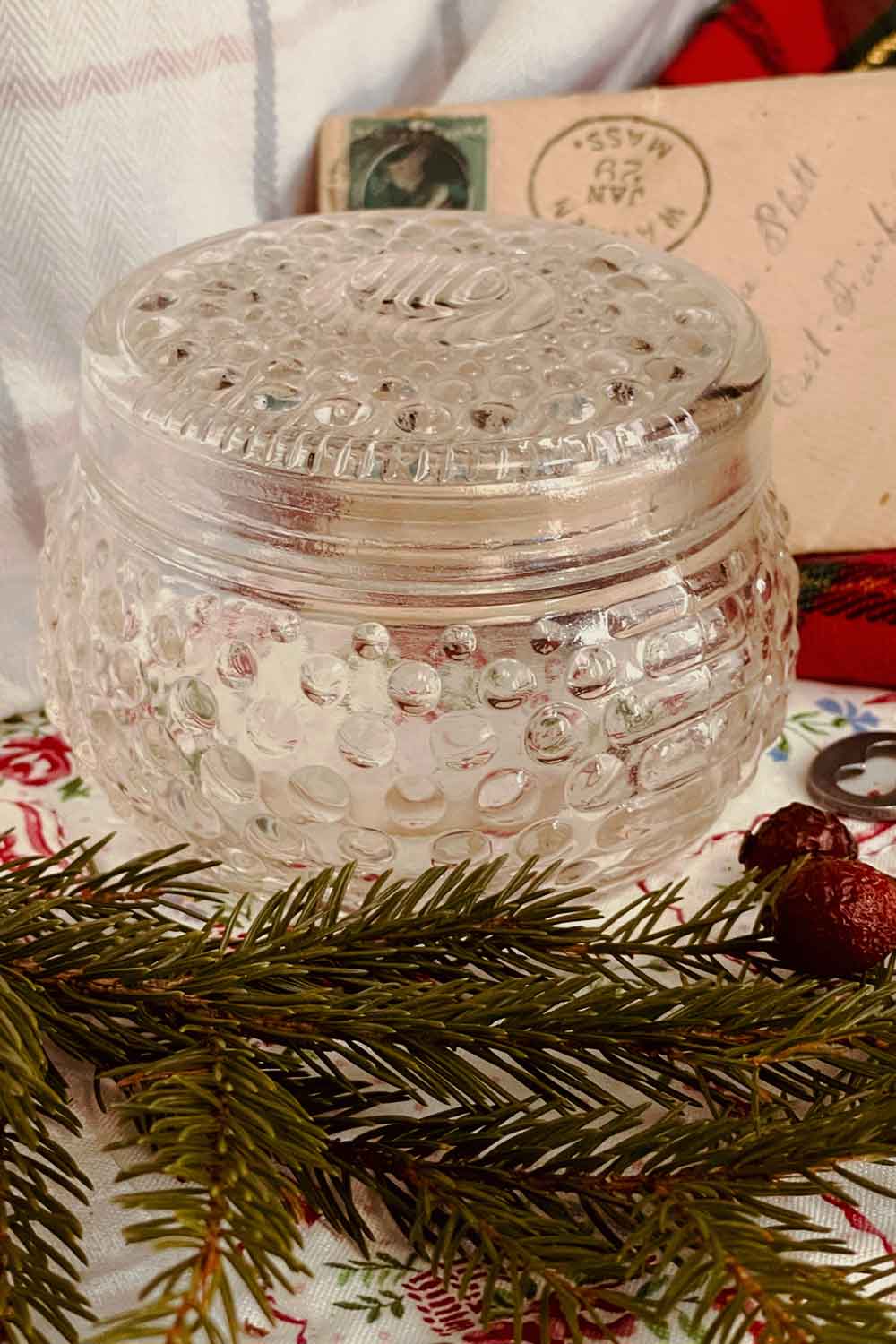 Vintage hobnail powder dish styled for Christmas with evergreen sprigs and old letters — a charming holiday body powder gift.