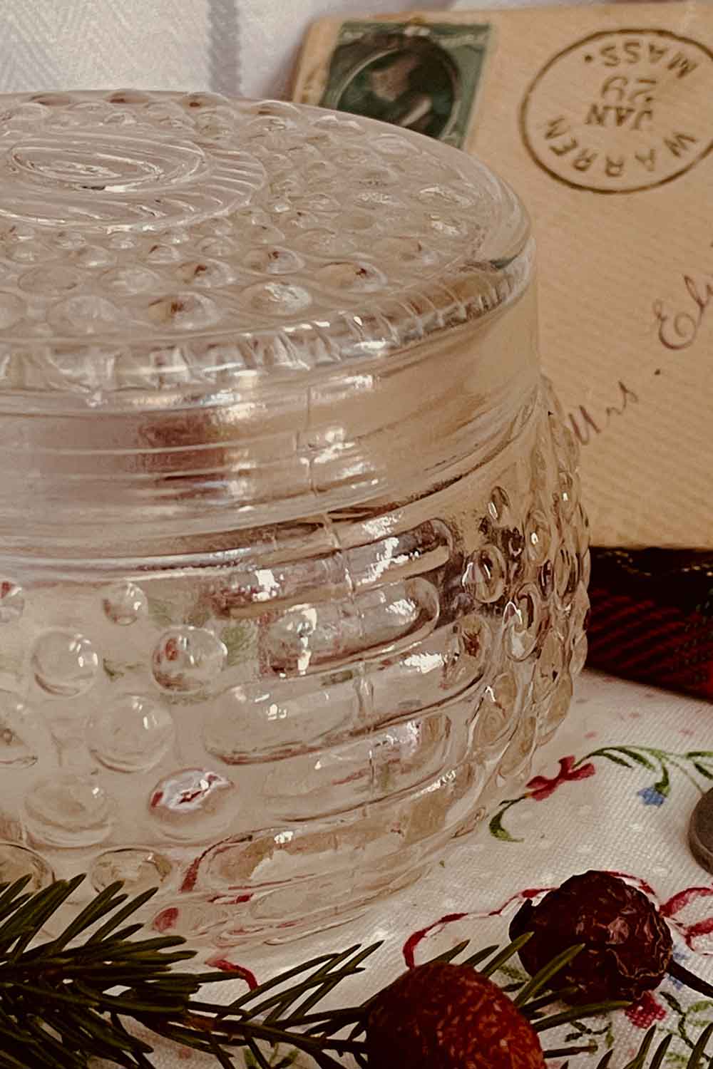 Clear vintage hobnail glass powder dish with lid, styled with evergreen sprigs and holiday linens — a sweet beginner piece for a new powder ritual.