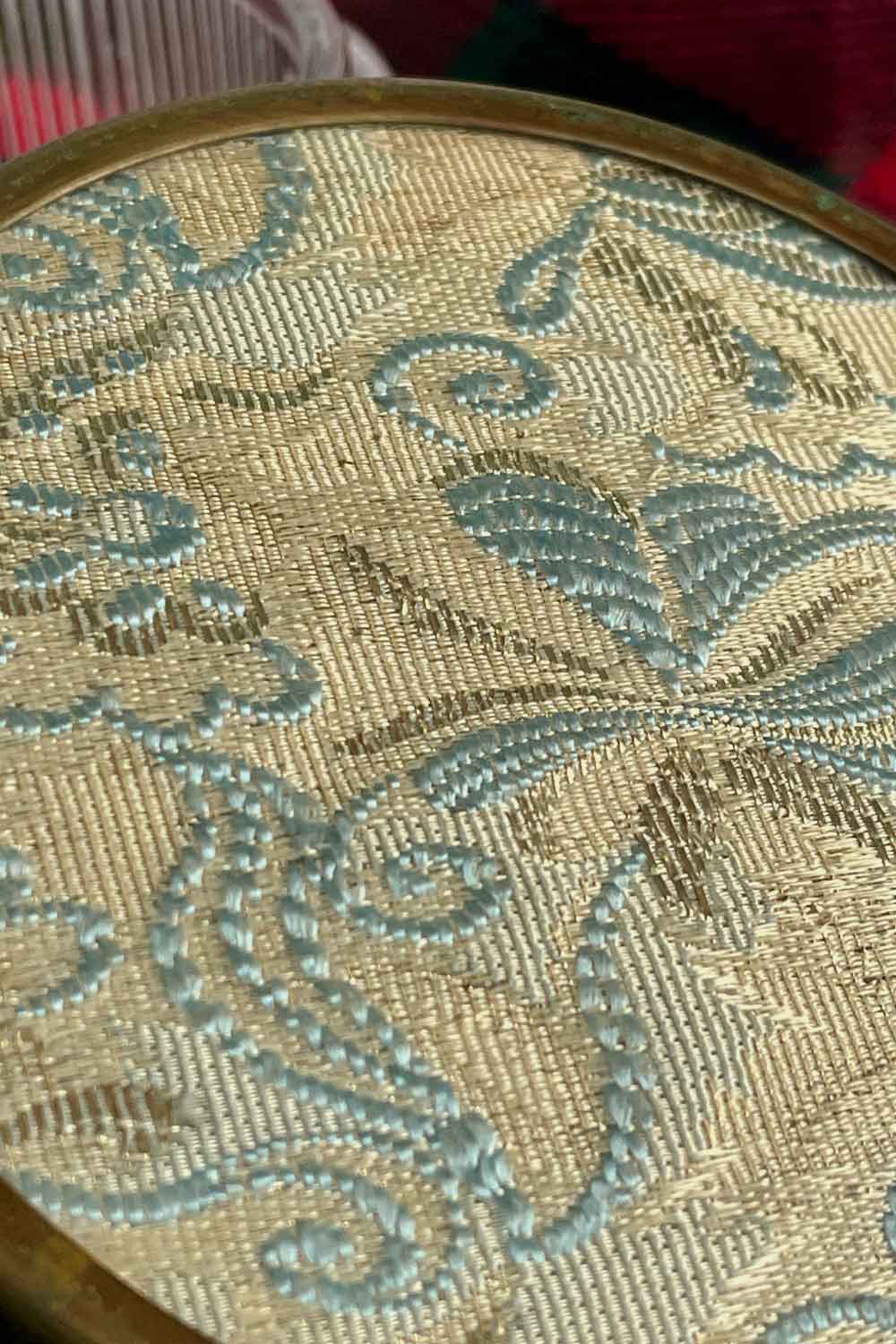 Detailed close-up of vintage Jacquard powder dish lid showing pale blue floral embroidery and woven gold base
