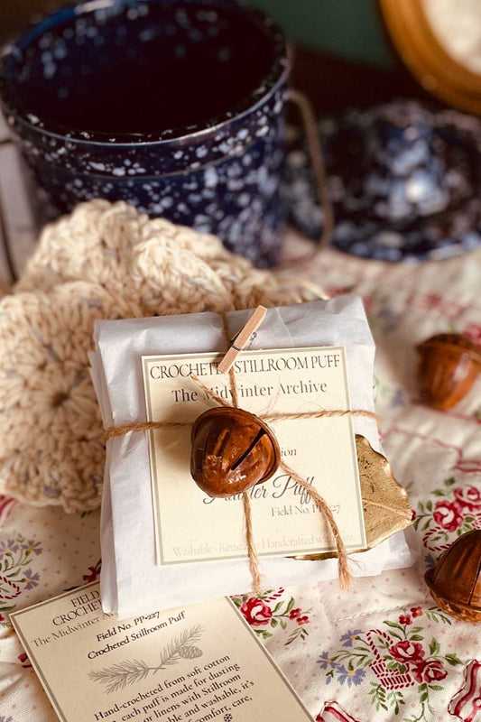 Crocheted Stillroom Powder Puff set wrapped in parchment tissue, tied with twine and an acorn bell — a handmade Christmas gift from the Stillroom.
