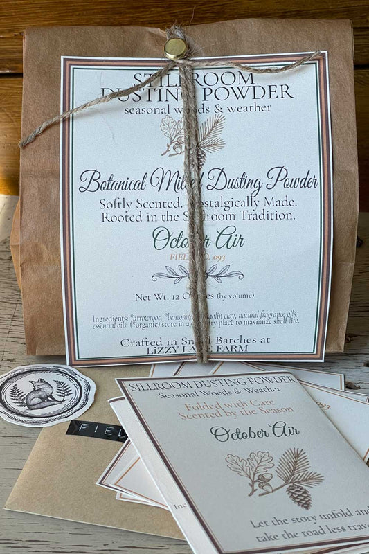 Bulk packaging of October air dusting powder and archival edition cards resting on a rustic surface.
