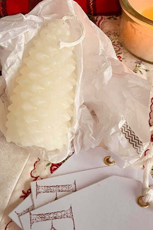 White beeswax pinecone candle wrapped in archive tissue with silver washi and hand-stamped gift tags — a nostalgic, limited-edition Midwinter Archive holiday gift.