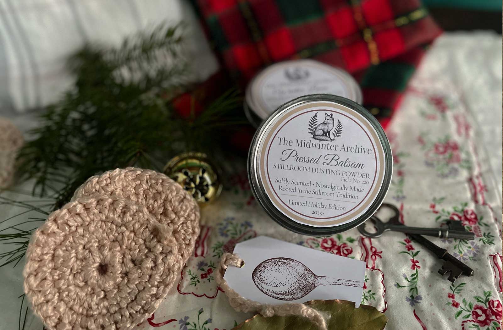 Pressed Balsam winter dusting powder in a holiday gift setting with quilt, greenery, and handmade puffs — Stillroom winter gift guide.