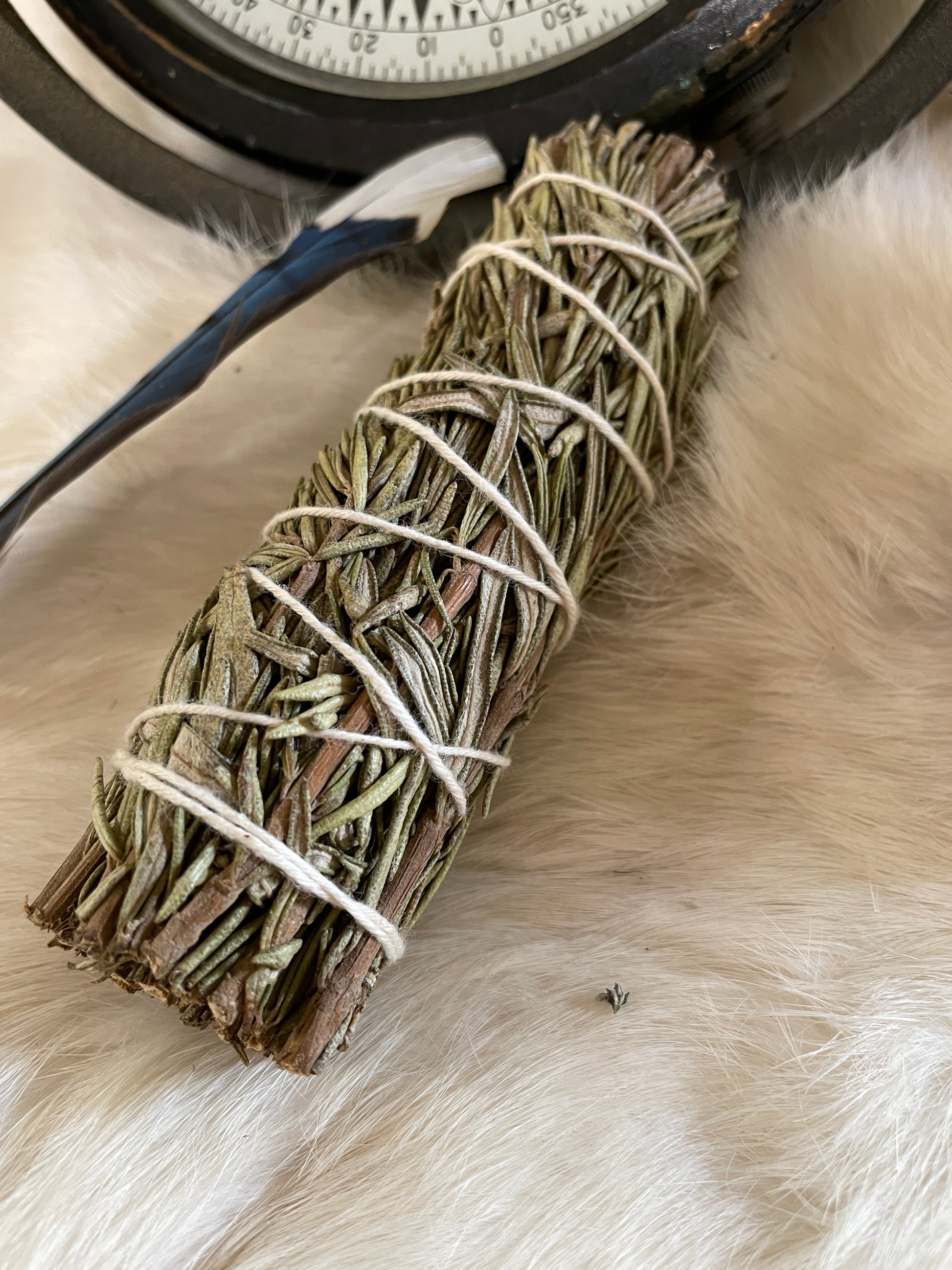 A small hand-tied rosemary smudge bundle resting on fur with soft lighting and vintage garden trimmings. The herbal texture and green tones are visible and calming.