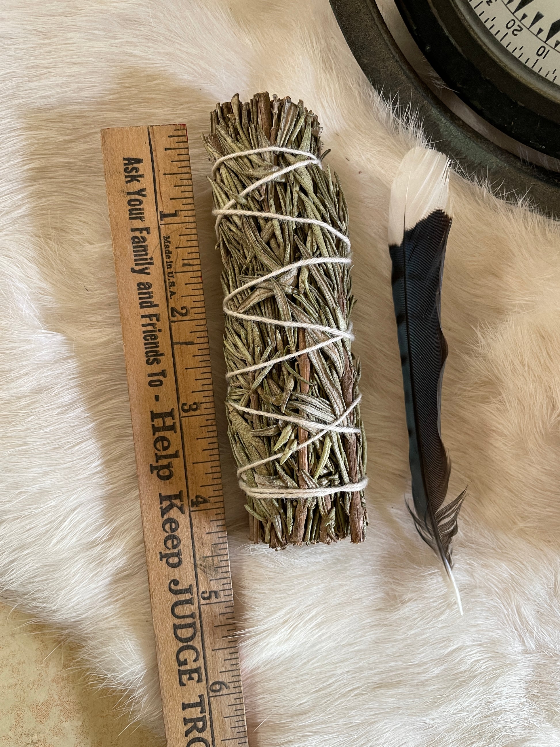 A small hand-tied rosemary smudge bundle resting on fur with soft lighting and vintage garden trimmings. The herbal texture and green tones are visible and calming.