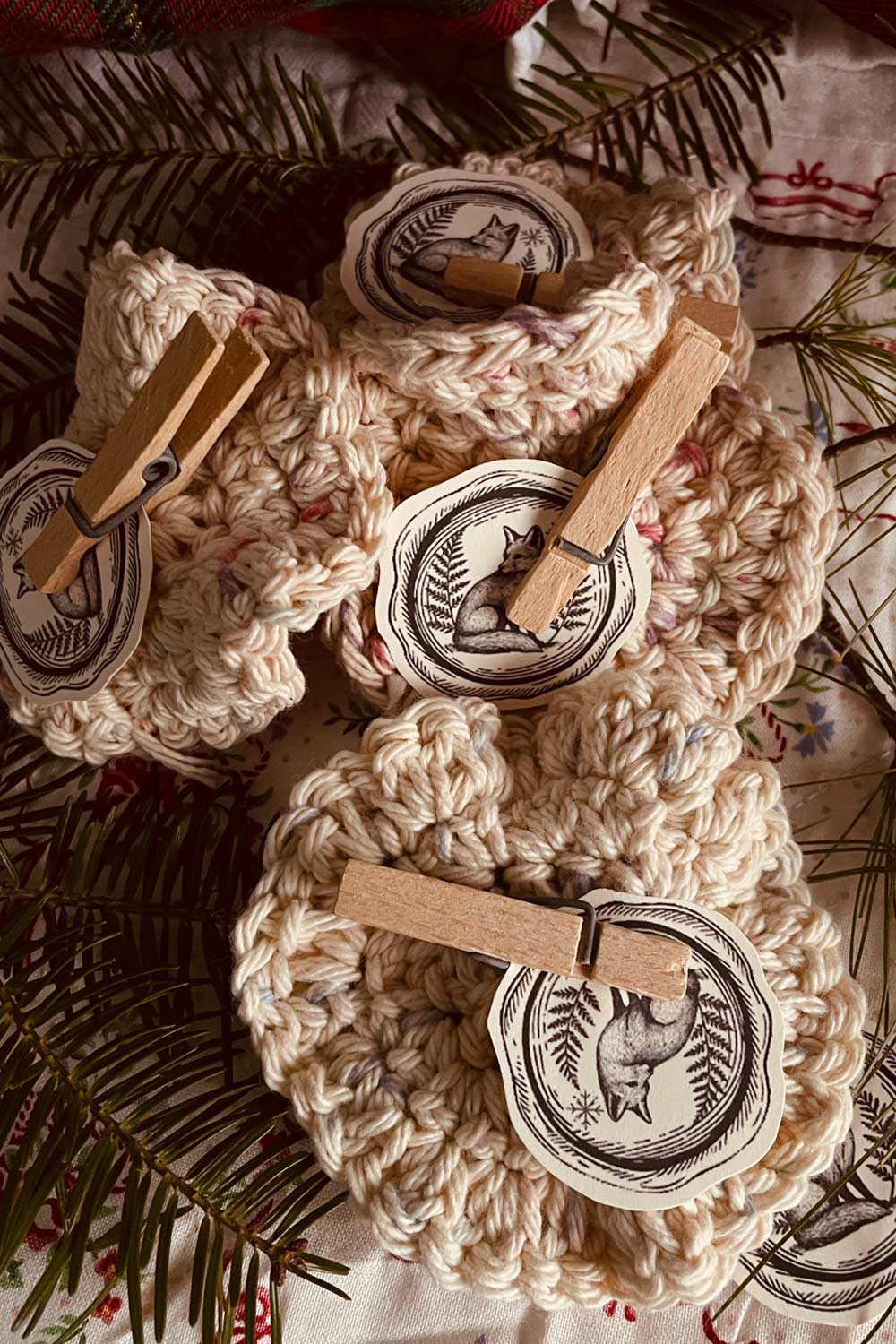 Hand-crocheted powder puffs with fox-seal tags and wooden clothespins — cottagecore handmade accessories for winter gifting.