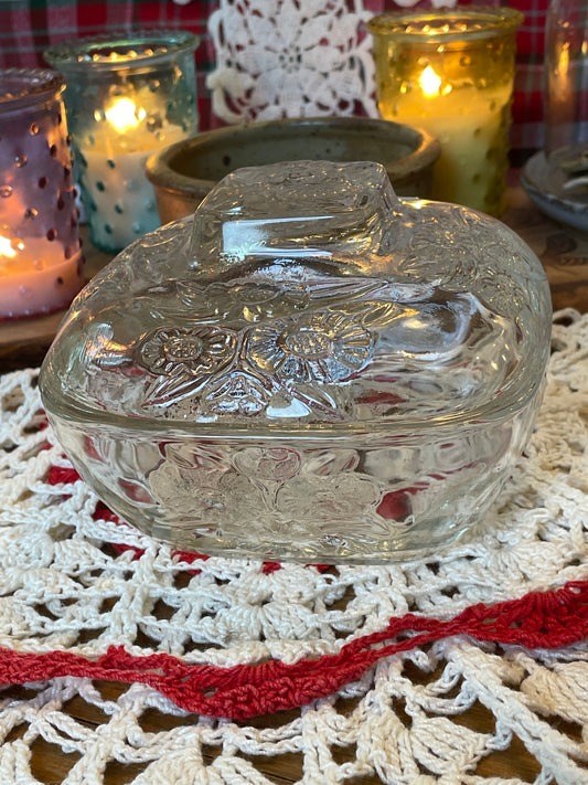 Vintage pressed glass powder dish with daisy motif, photographed on red and white crochet doily with lit candles in the background – top view showcasing lid detail.