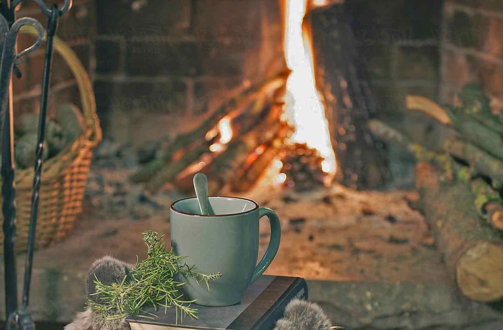 A steaming mug beside the hearth, rosemary sprig and soft light — the stillroom warmed by firelight