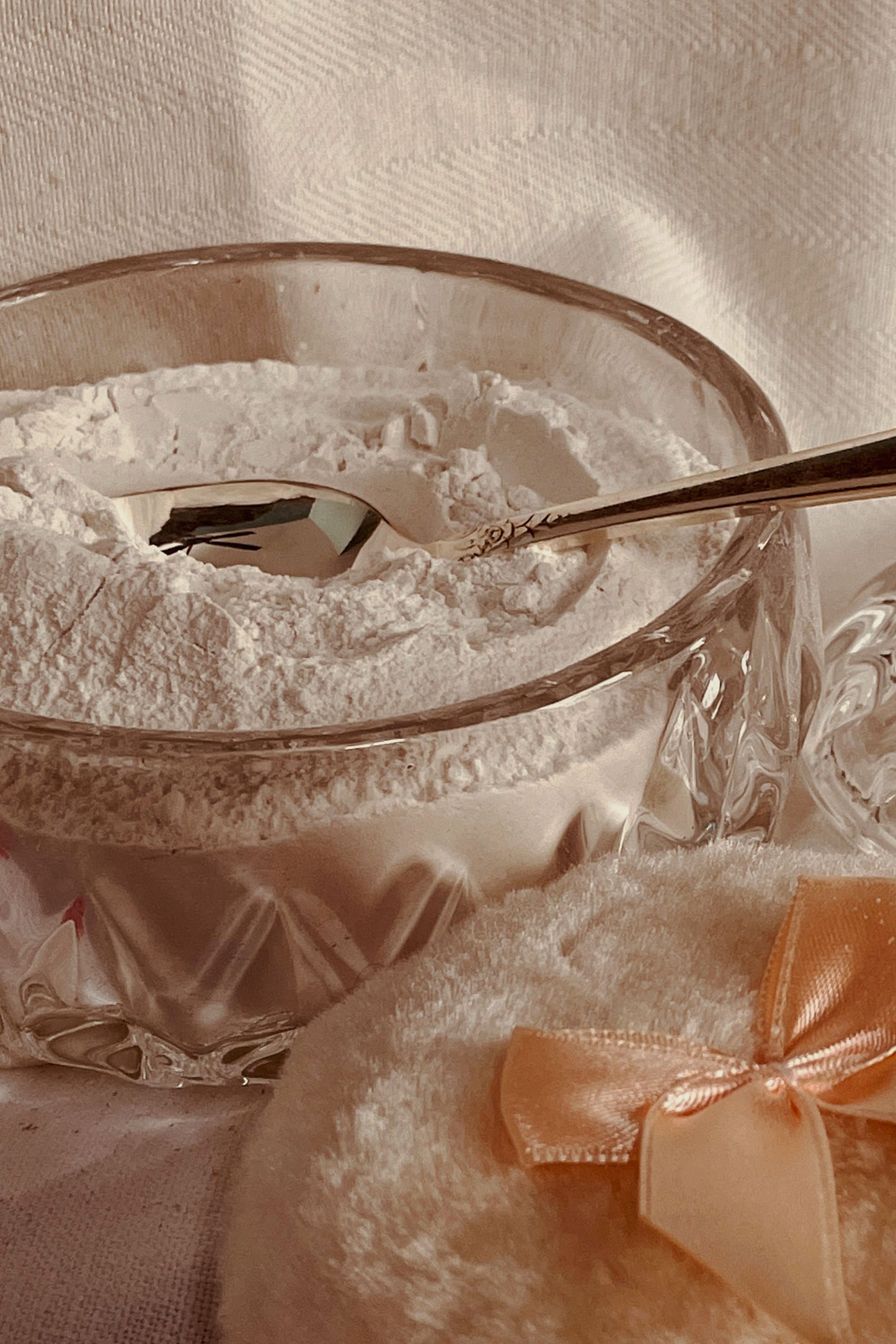 Glass powder dish filled with traditional lavender dusting powder and silver spoon resting in finely milled body powder