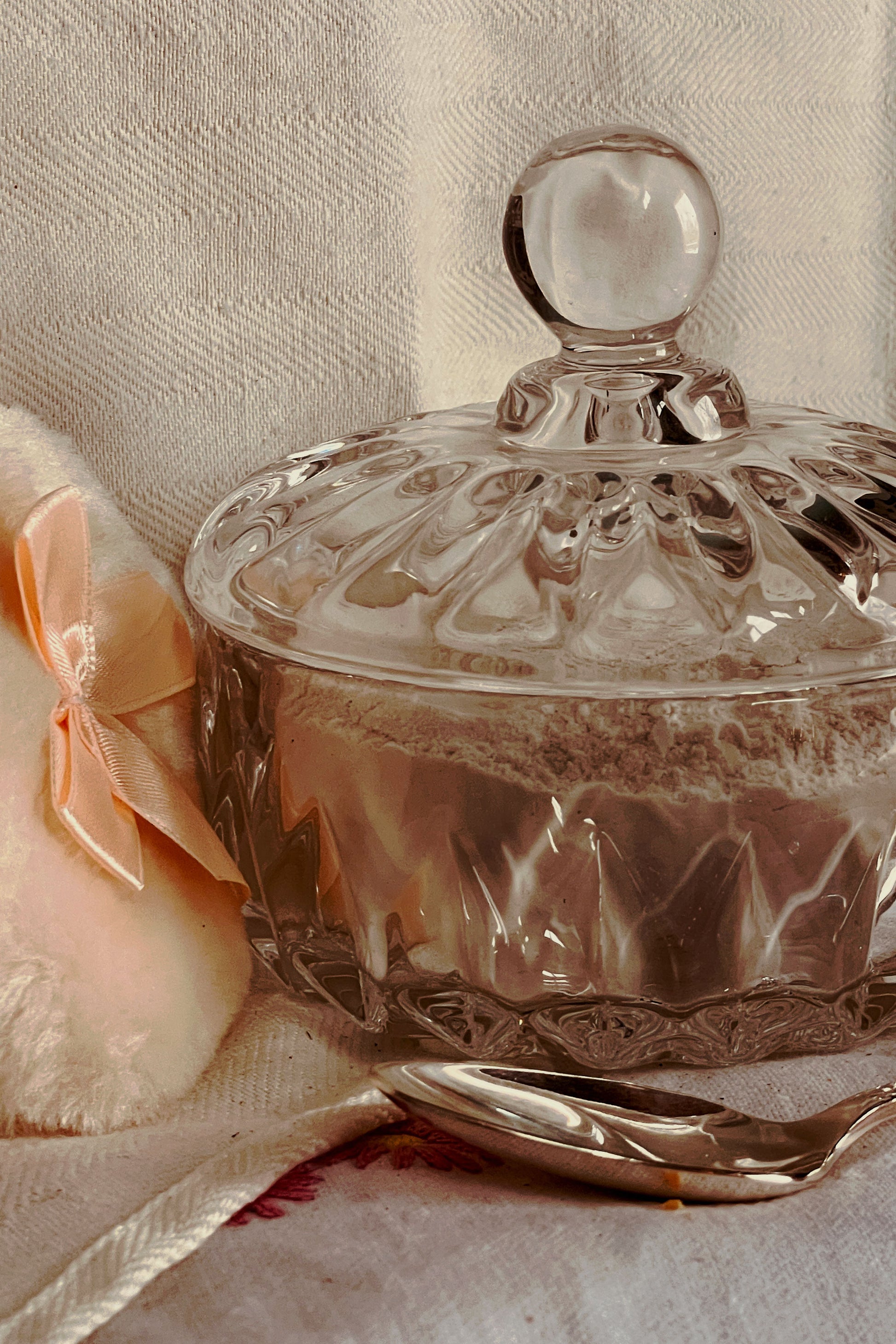 Glass powder dish with lid beside soft powder puff, part of a stillroom-made vanity powder dish set