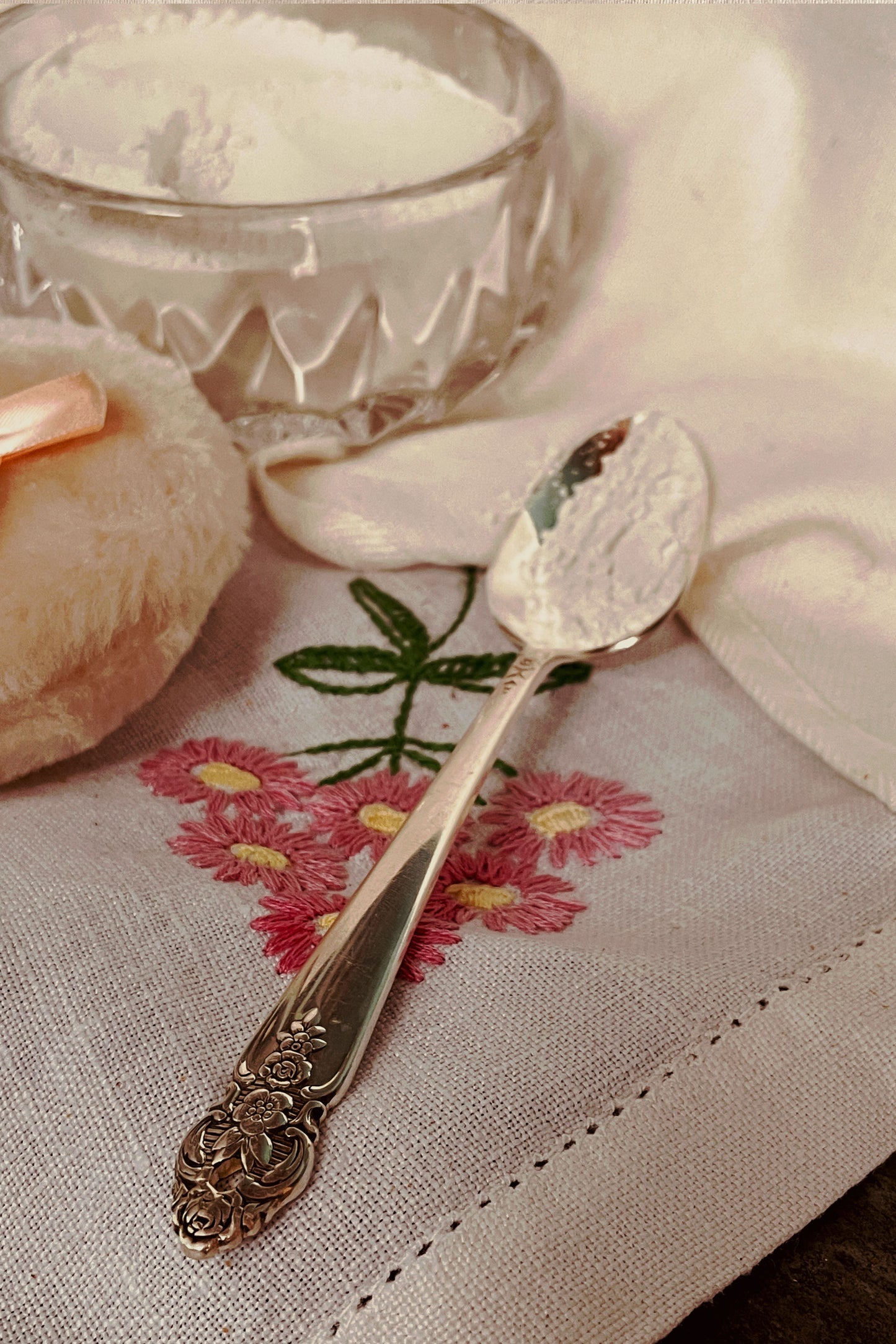 Silver spoon with lavender dusting powder beside soft powder puff on linen, vanity powder dish set detail