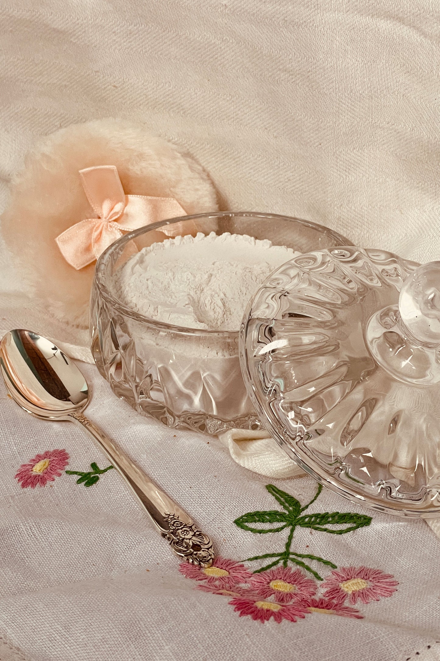 Stillroom-made powder dish set with glass vanity dish, lavender dusting powder, spoon, and puff arranged on linen