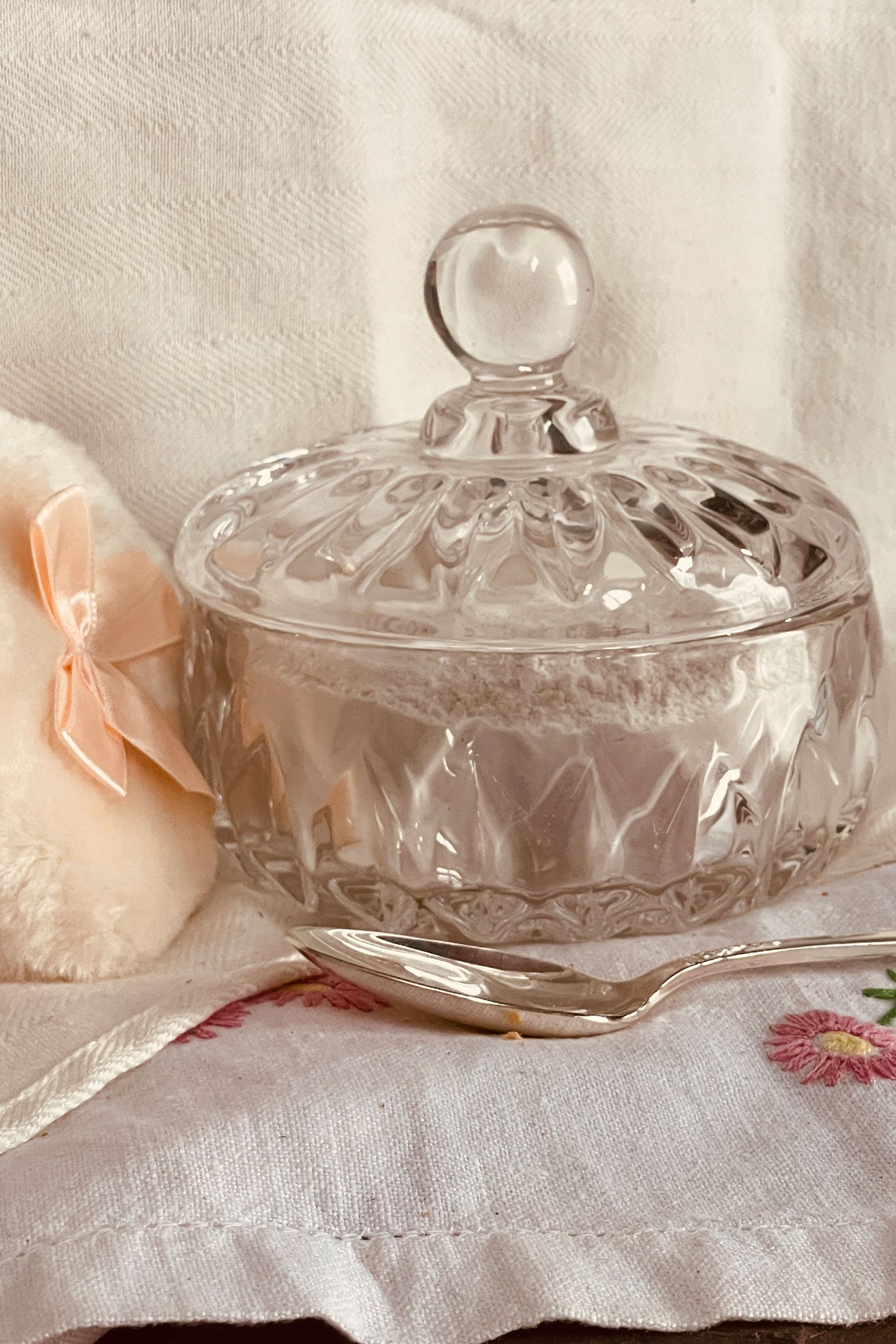 Glass powder dish with lid beside soft powder puff, part of a stillroom-made vanity powder dish set