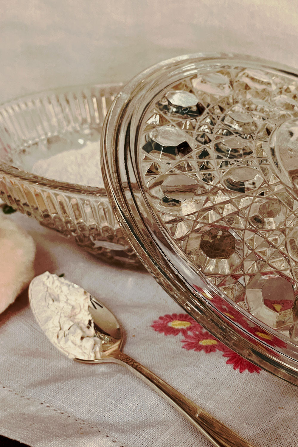 Open Button & Cane powder dish filled with lavender dusting powder, silver spoon resting beside the dish on linen.