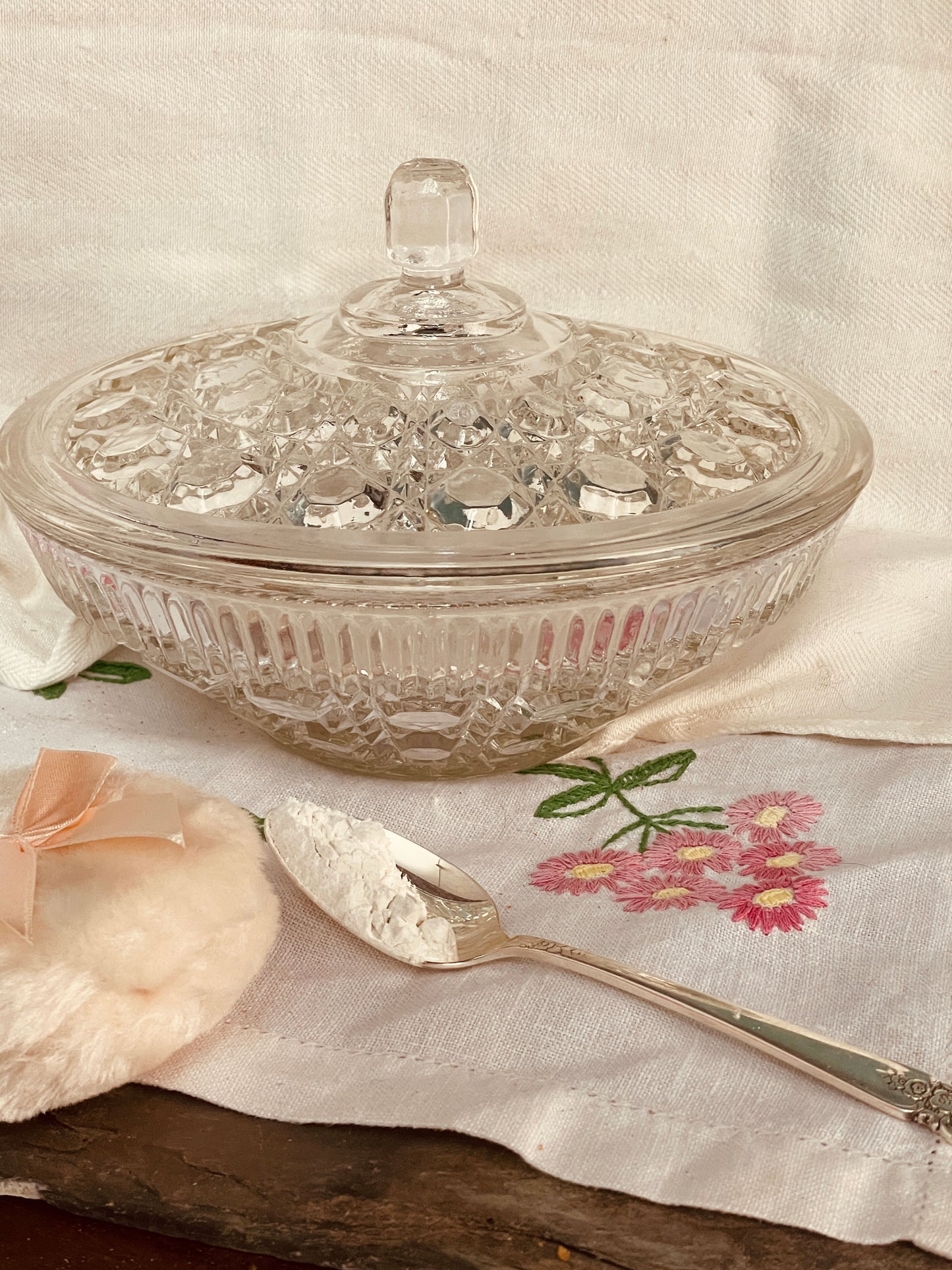 Vintage Button & Cane glass powder dish with lid, silver powder spoon, and soft powder puff arranged on an embroidered linen cloth.