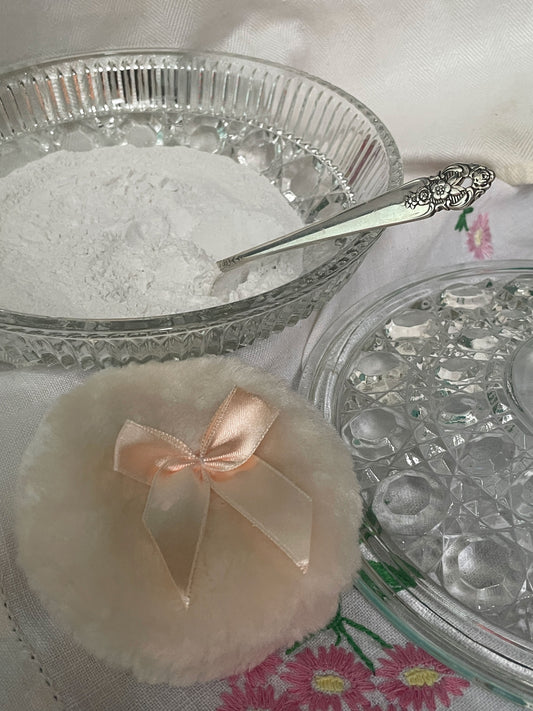 Interior view of vintage glass powder dish with lavender powder settled inside and spoon resting within the bowl.