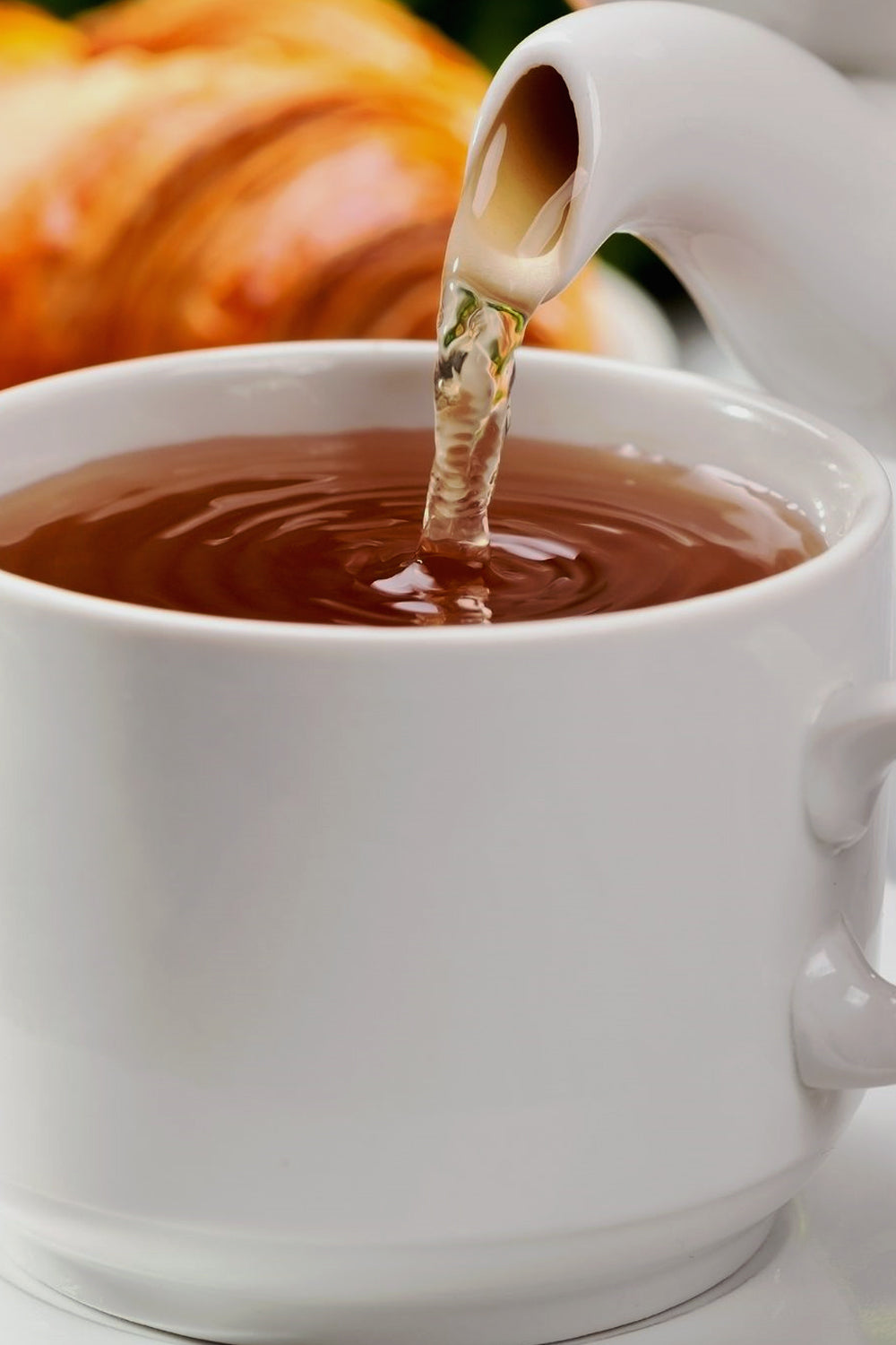 Steaming burdock tea being poured from a white teapot into a delicate tea cup, capturing the soothing ritual of herbal tea preparation.
