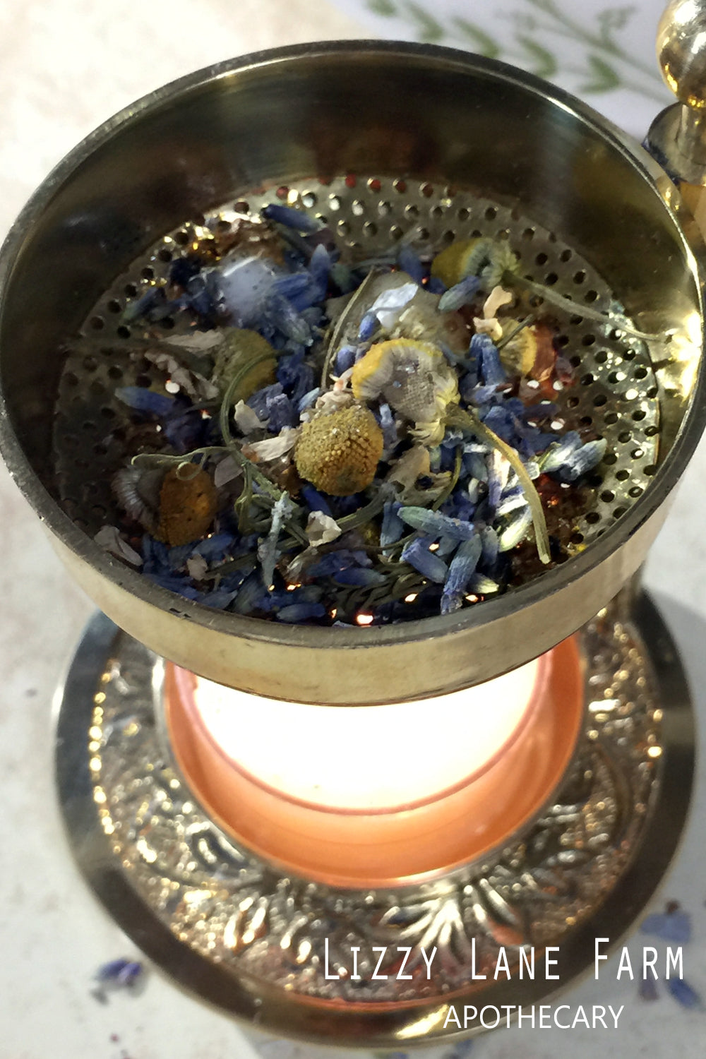 A brass incense burner filled with Drifting Away Herbal Incense, featuring chamomile and lavender buds. A gently flickering tea light candle warms the blend, allowing the herbs to smolder and release their calming, soothing aroma. Perfect for creating a tranquil atmosphere in your home.